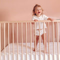 A baby smiling and standing in a crib with a Slumber Cloud Core Mattress Protector - Crib