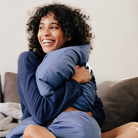 A young woman laughing and holding a Slumber Cloud pillow with an Essential Pillowcase on it